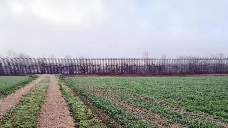 A field leading to a tall border fence