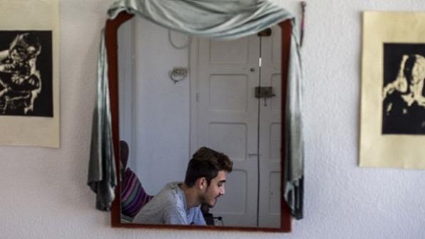 A Syrian refugee reflected in a mirror teaching Arabic via Skype