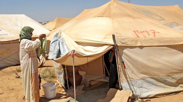 Syrian refugee woman hangs laundry in front of her tent in Za'atari camp in Jordan 